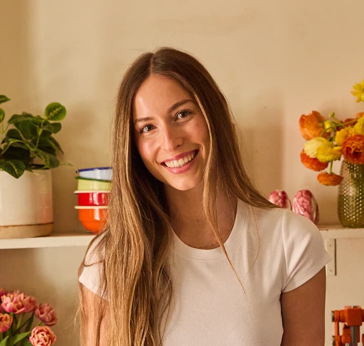 A warm interior featuring orange and yellow flowers in glass vases, stacked bowls in bright colors, and pink tulips on a counter.