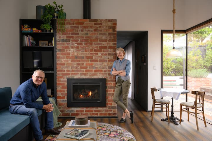 Two people in a cozy living room with a brick fireplace.