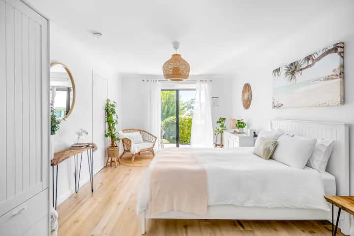 Bright bedroom with white decor, wooden accents, and garden view.