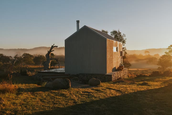 Small cabin in a misty rural landscape at sunrise.