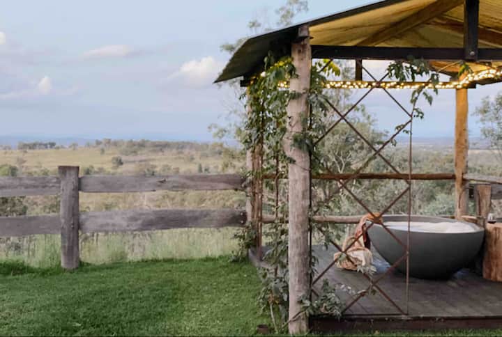 Outdoor bathtub under a rustic pergola with countryside views.