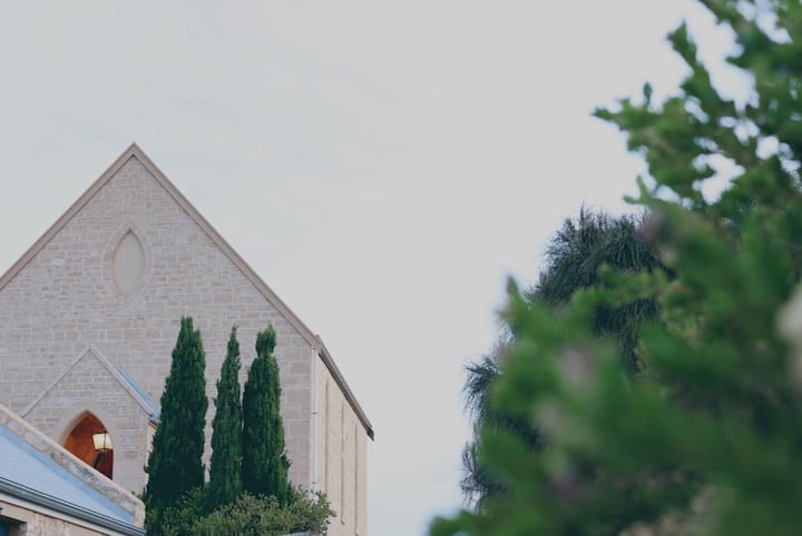 Stone church with tall trees in front and a cloudy sky.