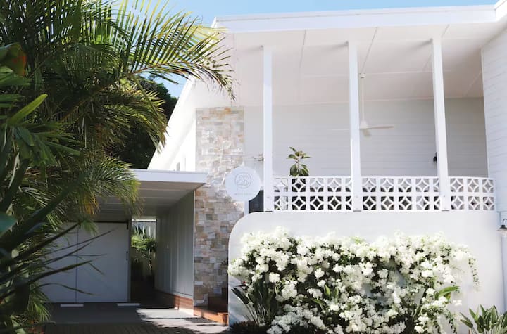 Modern white house with stone accents, palm trees, and flowers.