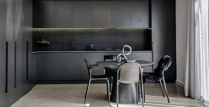 Sleek black kitchen with minimalist dining area and modern decor.