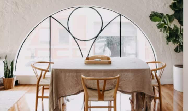 Dining area with arched window, wooden chairs, and linen-covered table.
