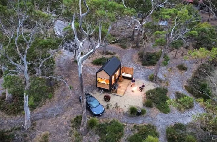 Tiny cabin in the woods with people gathered around a fire pit.