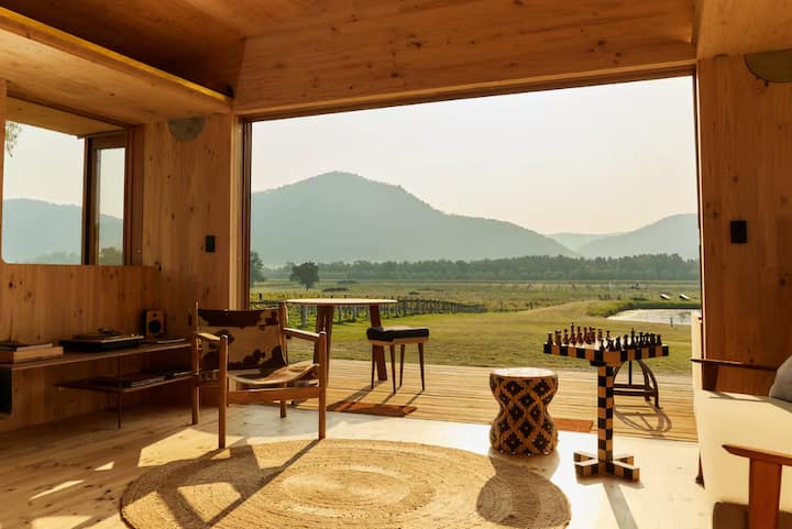 Wood-paneled cabin interior with open view of mountains and fields.