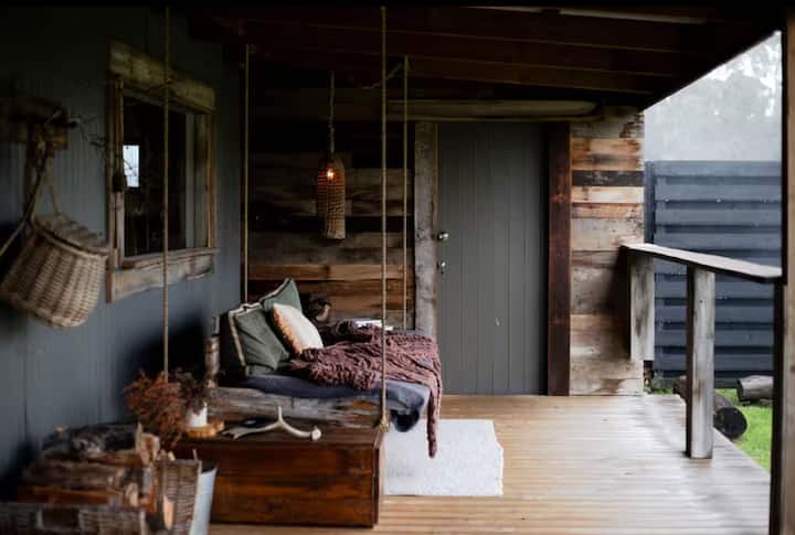Rustic porch with a hanging daybed, wooden accents, and cozy decor.