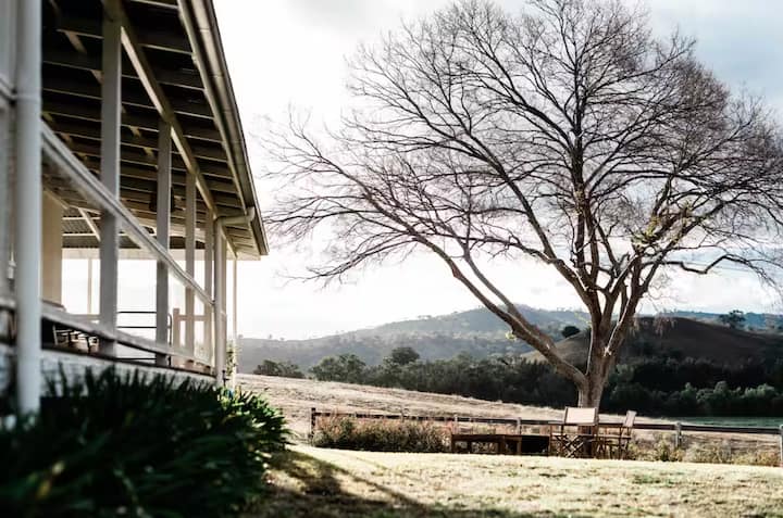 Rural farmhouse porch with mountain views and a large bare tree.