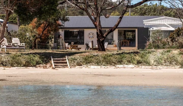 Beachfront house with outdoor seating, trees, and direct access to the water.