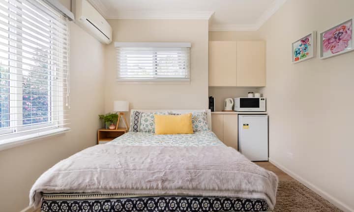 Compact studio bedroom with kitchenette and bright bedding