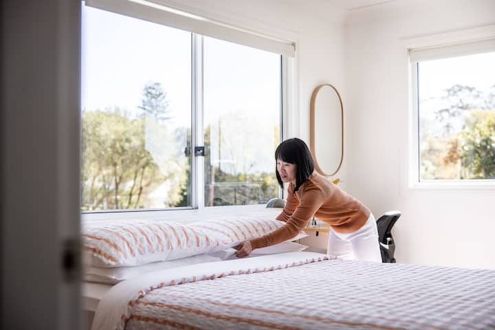 Woman making bed in bright bedroom