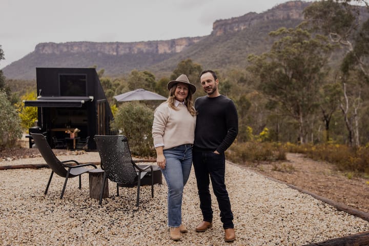 Couple standing outside of a tiny home with cliffs in background
