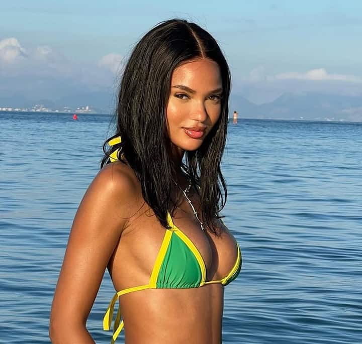 A vibrant scene at Copacabana Beach in Rio de Janeiro, featuring a person in a green and yellow bikini with the ocean and hazy mountains in the distance.