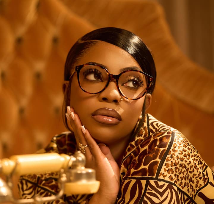 A stylish setting featuring warm, golden tones with a tufted leather backdrop and an intricate patterned scarf, alongside a vintage-style rotary phone in the foreground.