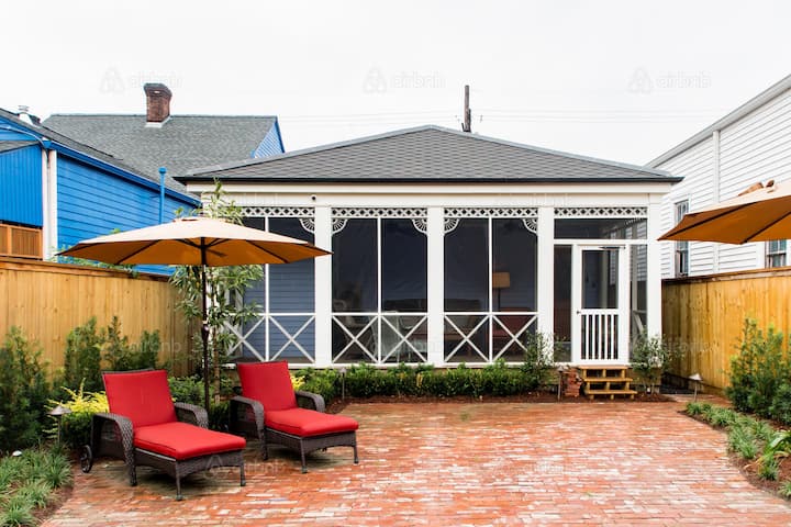 Cozy backyard space of an Airbnb rental with a screened porch, brick patio, two red lounge chairs, and yellow umbrellas, perfect for relaxing before or after an Atlanta Falcons game.