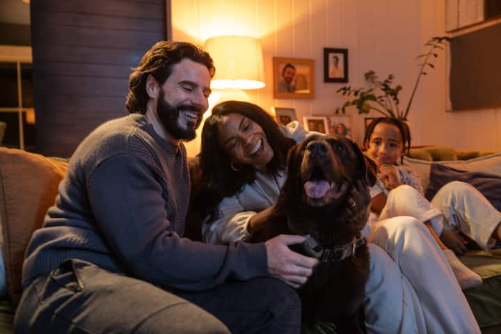 Mom, dad, son and dog watching TV on couch at home