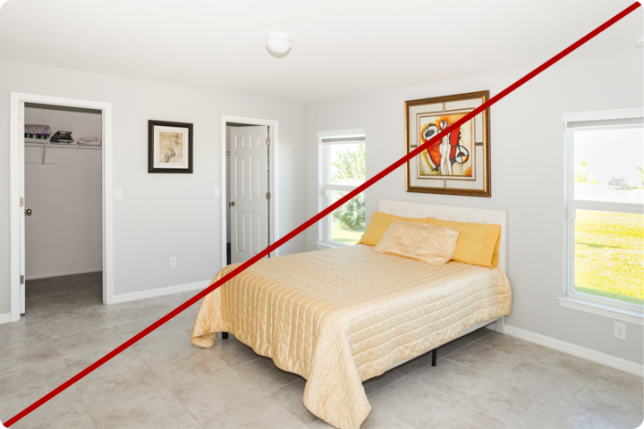 Chambre lumineuse et minimaliste avec un lit queen size soigneusement fait, des draps et des oreillers jaunes, deux fenêtres laissant entrer la lumière naturelle et une porte de placard sur la gauche. Une ligne diagonale rouge traverse l'image, indiquant une comparaison ou une exclusion.