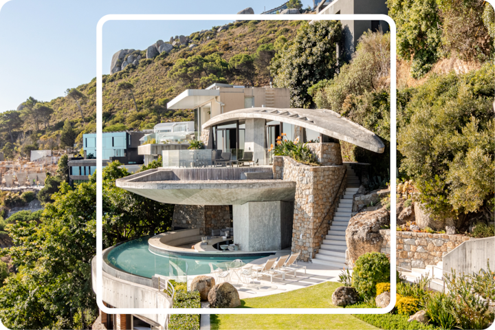 Villa de luxe à flanc de colline entourée de verdure, dotée d'une piscine à débordement incurvée et d'une architecture moderne avec de grandes fenêtres et des murs en pierre.