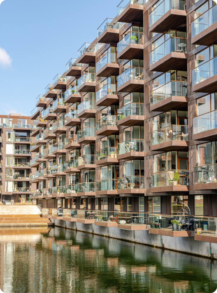 Immeuble moderne avec des balcons en verre donnant sur un canal serein par une journée ensoleillée.