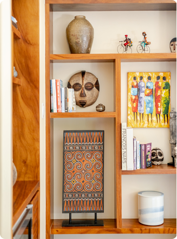 Étagère en bois avec une décoration éclectique : œuvres d'art abstraites aux couleurs vives, tableaux à motifs d'inspiration tribale, vases en céramique et livres.