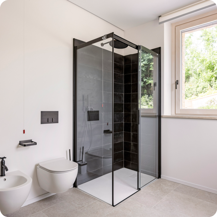 Salle de bain moderne avec une douche à l'italienne au carrelage noir, un siège intégré et une douchette à main. On peut également voir des toilettes et un bidet muraux, une tirette et une grande fenêtre offrant une lumière naturelle.