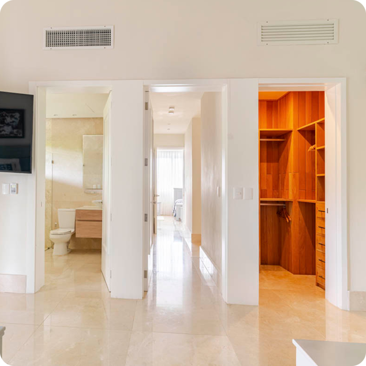 Couloir intérieur lumineux aux sols polis couleur crème, présentant trois portes ouvertes donnant sur une salle de bain, une chambre et un dressing lambrissé.