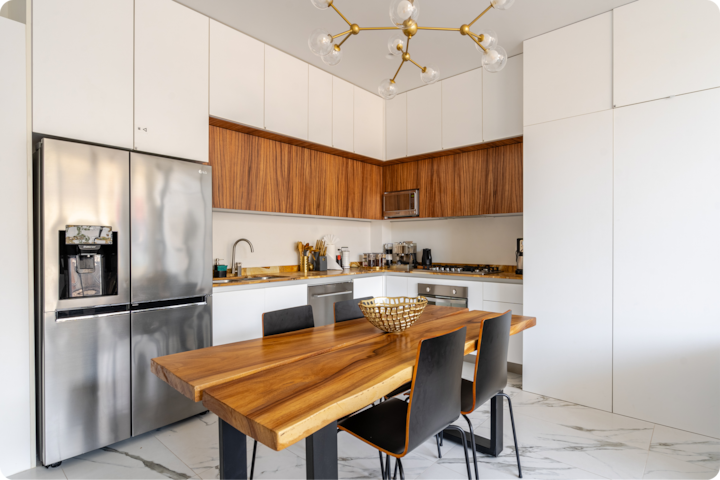 Cuisine moderne avec des placards blancs, des détails en bois, un réfrigérateur en acier inoxydable et une table en bois entourée de chaises noires.