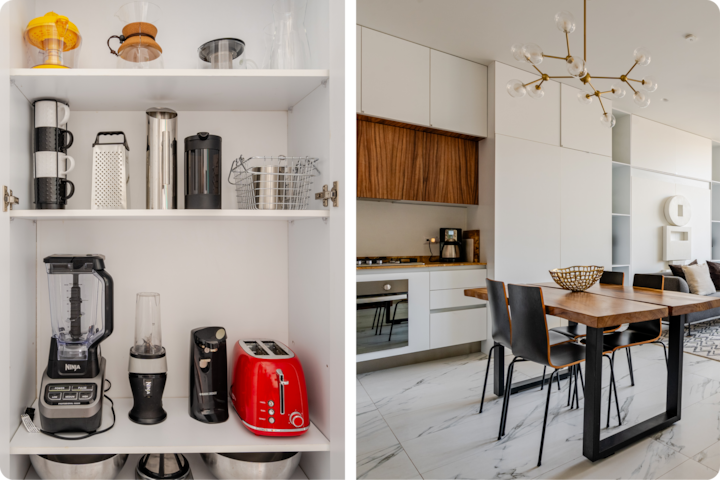 Une cuisine moderne avec une table noir et bois pour 4 personnes, à côté d'un meuble blanc avec des appareils de cuisine soigneusement disposés, dont un grille-pain rouge, un mixeur et de quoi préparer du café.