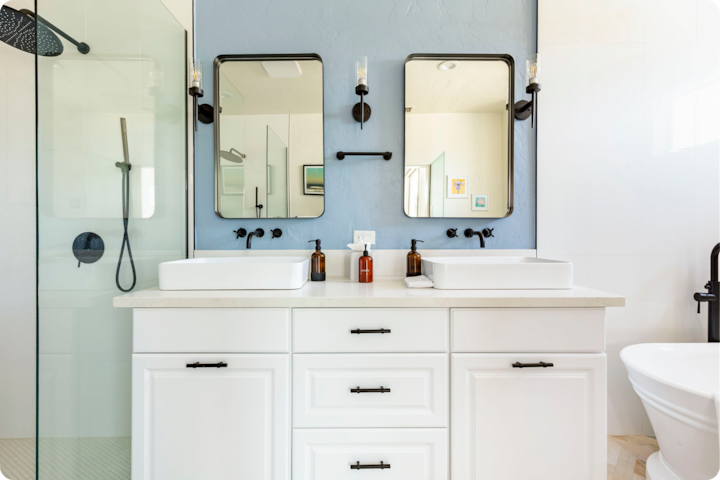 Salle de bain moderne avec deux lavabos blancs, des accessoires noirs, de grands miroirs, une cabine de douche vitrée et un mur bleu clair.