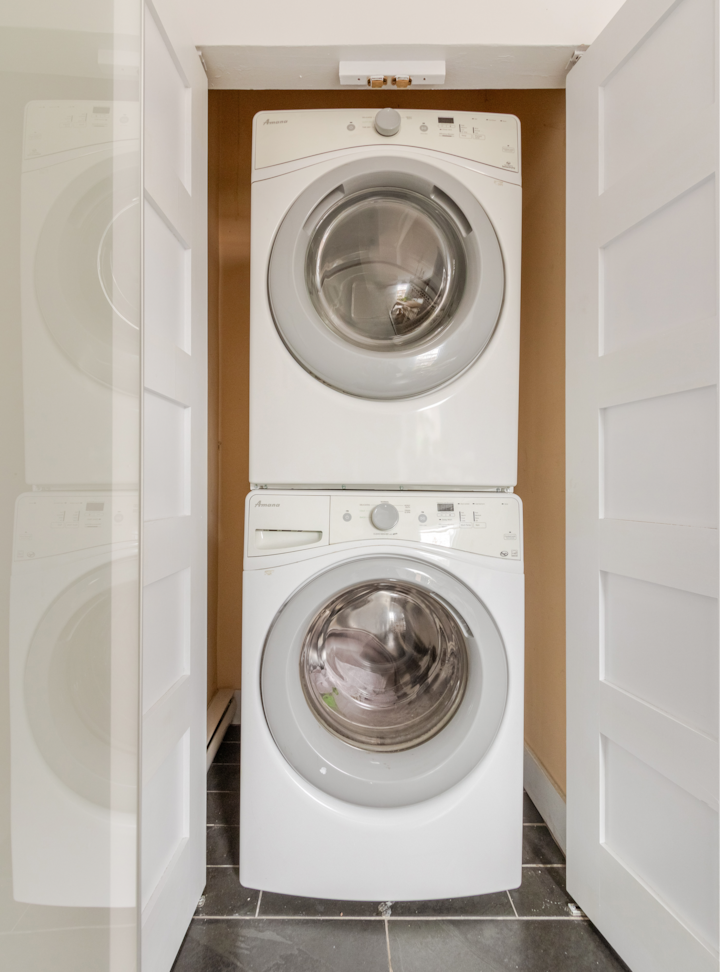 Lave-linge et sèche-linge empilés à l'intérieur d'un petit placard à linge avec des portes blanches, idéal pour les petits logements.