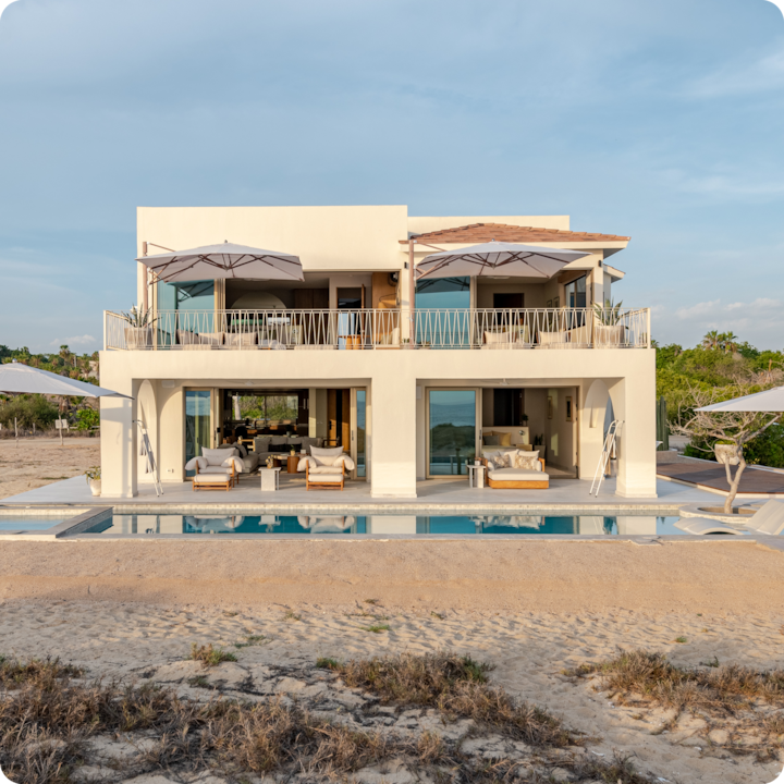 Villa moderne de deux étages en bord de mer avec de grandes fenêtres, une piscine et des coins salons extérieurs, le tout baigné d'une lumière douce de fin d'après-midi.