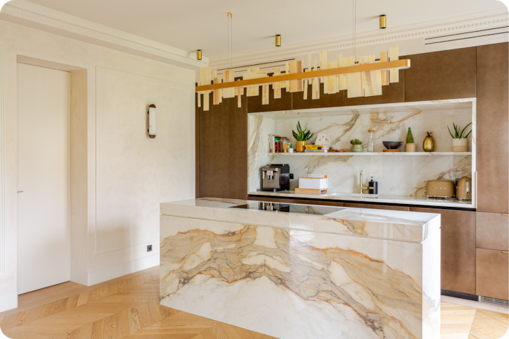 Cuisine moderne avec îlot en marbre blanc veiné de marron, étagères ouvertes dotées de plantes et d'objets de décoration, et suspension en bois au design géométrique.