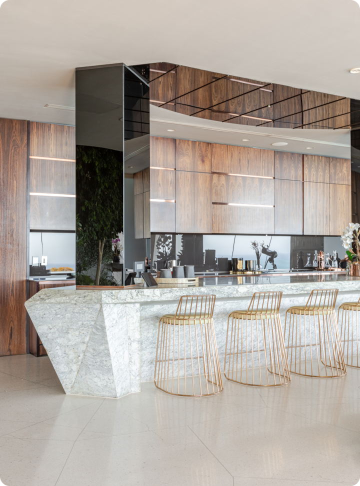 Cuisine moderne avec des placards en bois, un îlot en marbre entouré de tabourets de bar en métal doré, des plantes décoratives et des appareils électroménagers élégants.