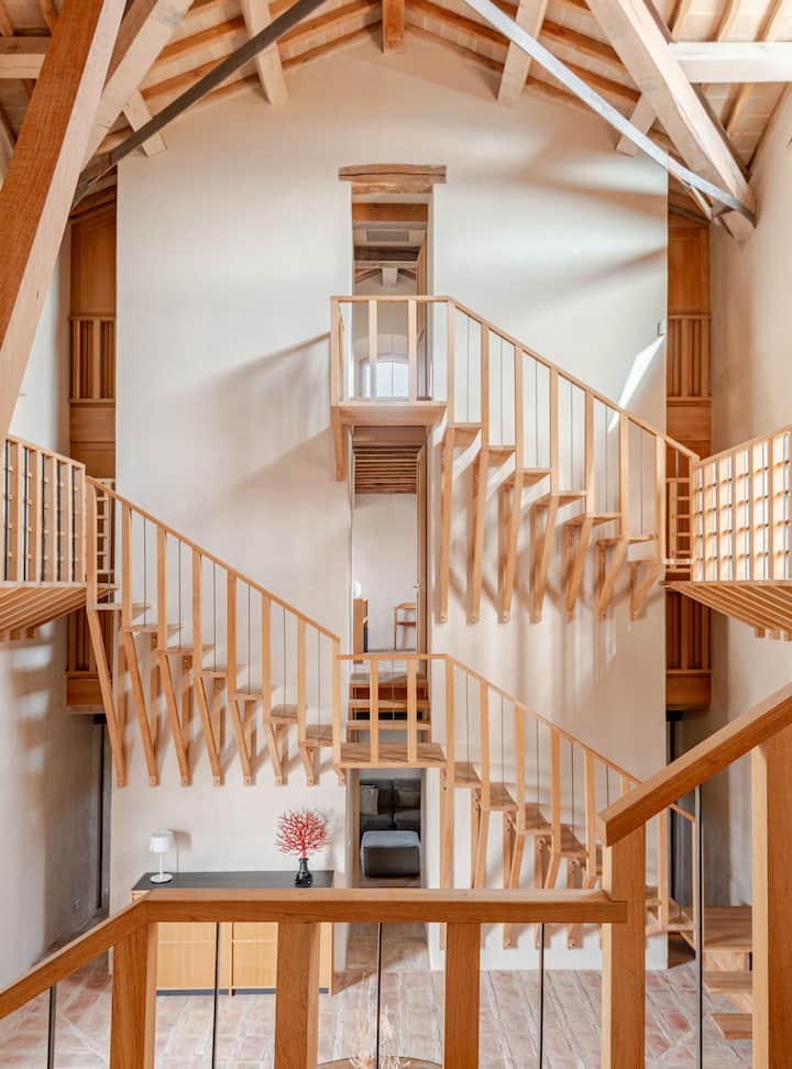 Photo d'un intérieur lumineux et moderne avec plusieurs escaliers en bois menant à différents niveaux surélevés sous un plafond voûté, mettant en valeur une architecture unique.