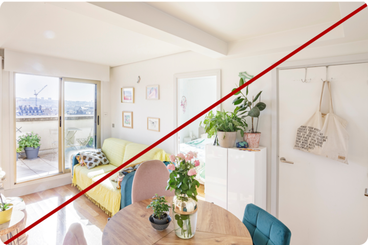 Un espace de vie lumineux et baigné de soleil avec un coin salon confortable au canapé doté d'un plaid jaune, une table ronde en bois avec des plantes en pot et un vase, et une grande baie vitrée menant à un balcon avec des plantes en pot. L'image est barrée d'une ligne rouge en diagonale afin de montrer que la photo n'a pas été prise à la bonne hauteur et ne met donc pas bien en valeur l'espace et la lumière naturelle de la pièce.