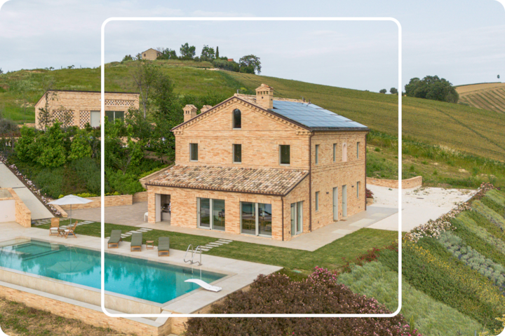 Vue aérienne d'une spacieuse villa en briques avec des panneaux solaires sur le toit, entourée de collines verdoyantes et de vignes. La propriété comprend aussi une grande piscine et un coin salon extérieur au premier plan.