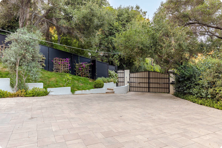 Une grande allée entourée de verdure, avec de grands arbres et un portail noir moderne en arrière-plan.