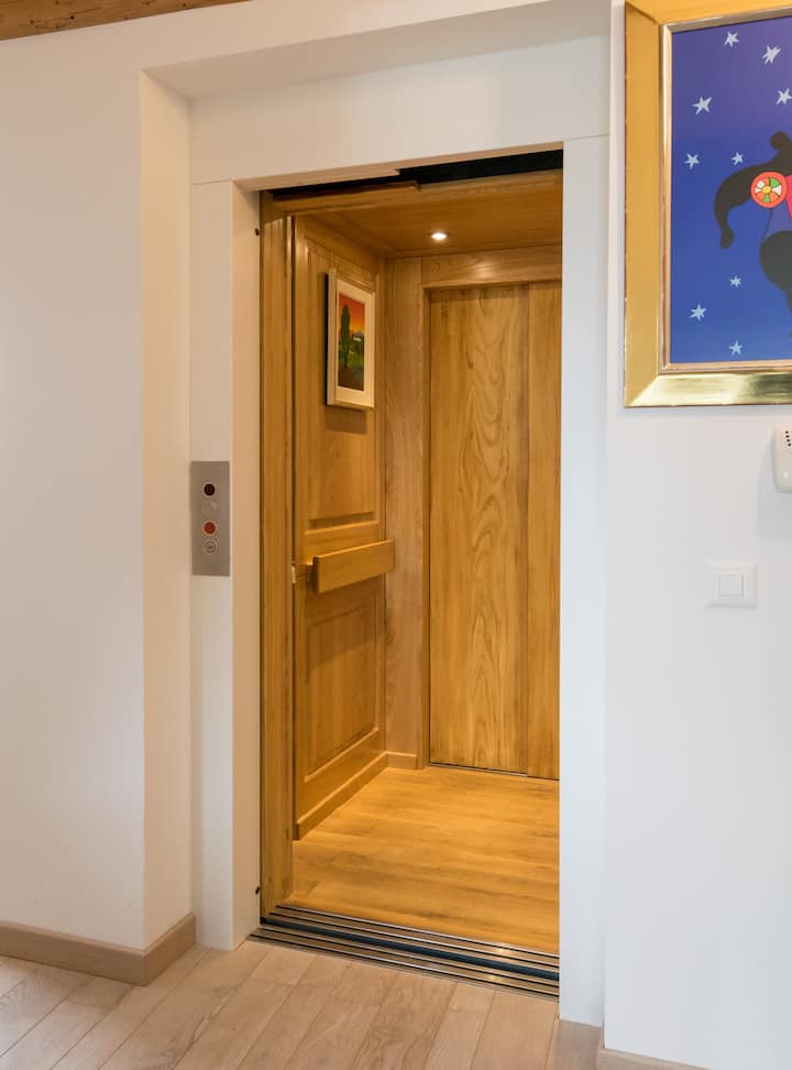 Un ascenseur dans un logement, avec des panneaux en bois, la porte ouverte, un éclairage intérieur et un tableau accroché sur une des parois.