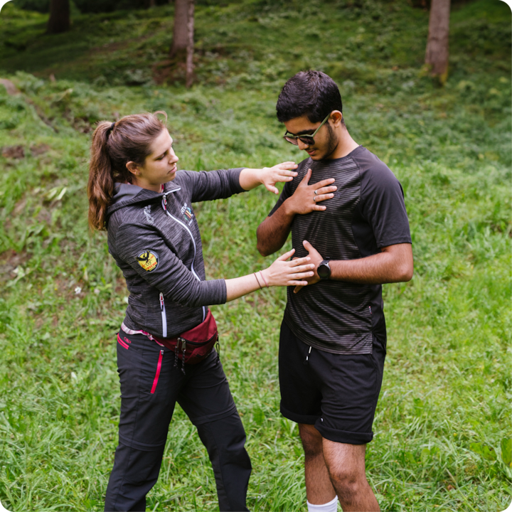 Une expérience en plein air dans une forêt verdoyante où une guide montre une technique de respiration ou de pleine conscience à un participant, qui place une main sur sa poitrine.