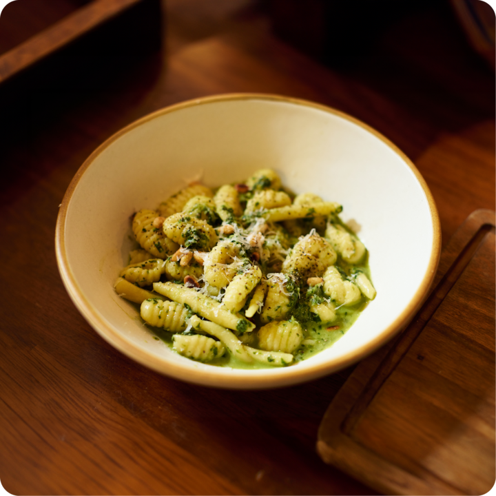 Sur une table en bois, un bol de gnocchi fraîchement préparés et agrémentés d'une sauce pesto crémeuse, de fromage râpé et d'herbes.