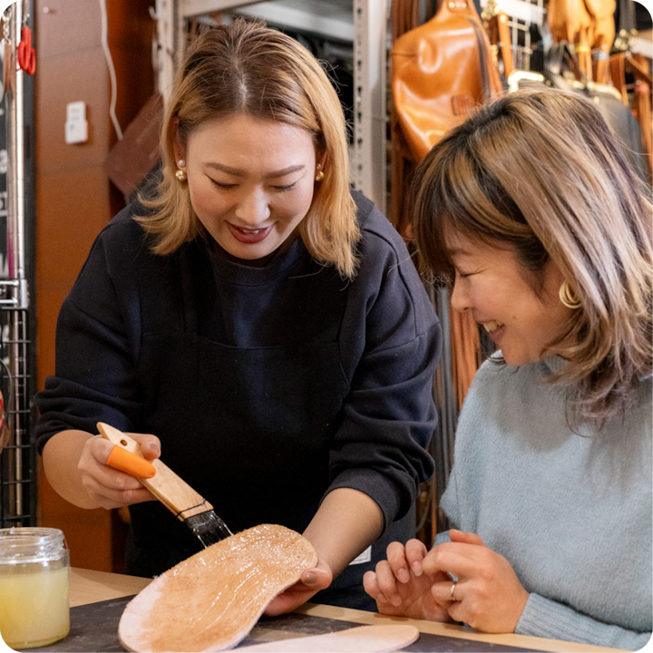 Lors d'un atelier autour du cuir, une personne montre comment brosser du cuir avec une substance transparente, tandis qu'une autre personne observe attentivement.