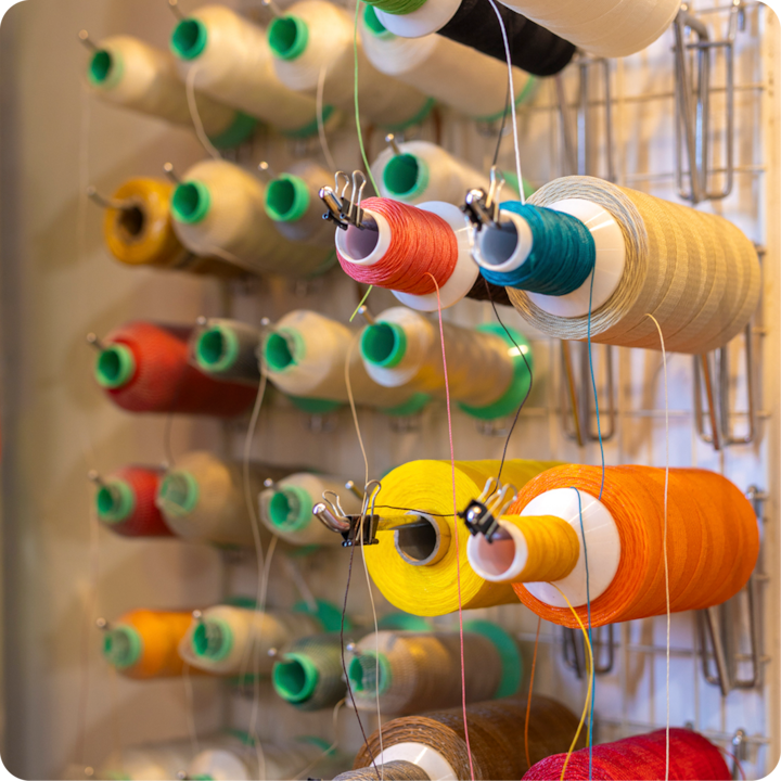 Plan rapproché d'un porte-bobine avec des bobines de couleurs vives dans des tons de jaune, orange, rouge, bleu sarcelle, parmi d'autres, évoquant un passe-temps manuel ou une activité artisanale.
