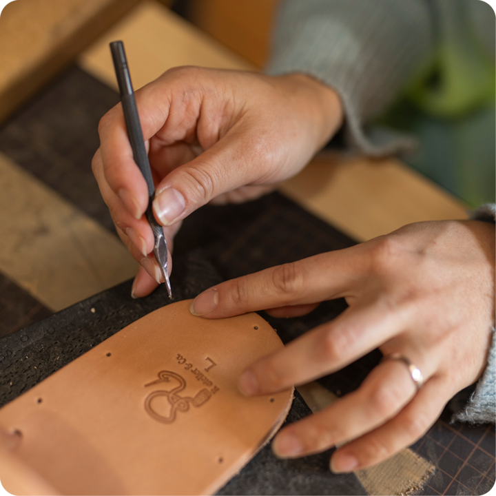Plan rapproché de mains gravant une pièce en cuir lors d'un atelier d'artisanat. Des détails de gravure sont visibles.
