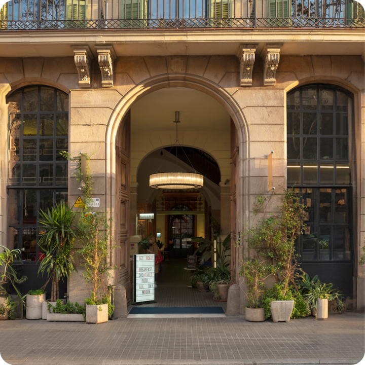 Entrée élégante d'un bâtiment historique avec de hautes arcades, une porte encadrée de verdure et un lustre diffusant une lumière chaleureuse à l'intérieur.