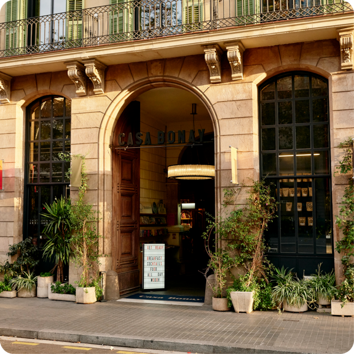 Vue de la façade de Casa Bonay, un bâtiment historique avec des portes cintrées en bois et de grandes fenêtres, entouré de plantes en pot et de verdure.