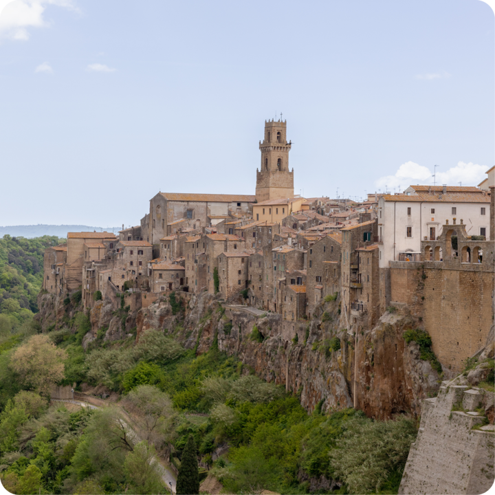 Une vue pittoresque d'un village rustique construit sur une colline rocheuse, encadré de verdure et d'une large portion de ciel.