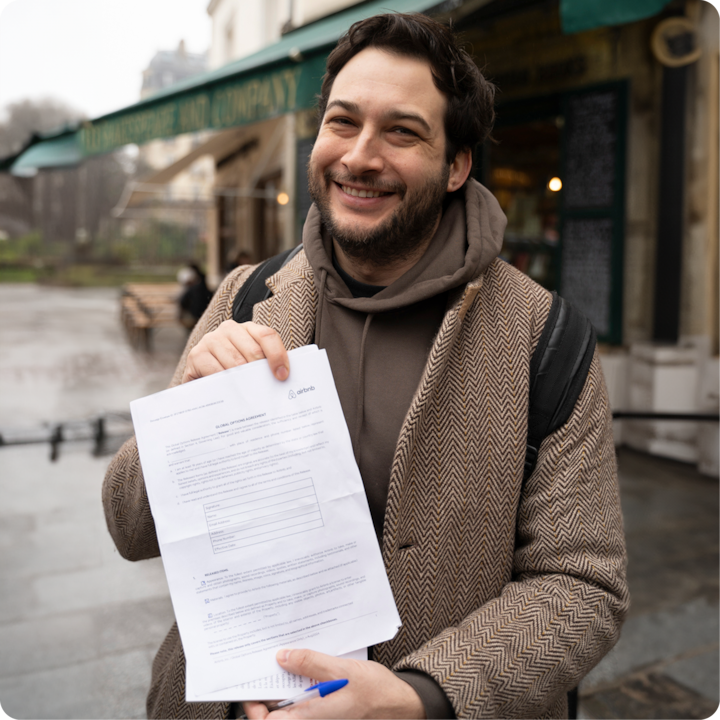Plan rapproché d'une personne montrant un formulaire de décharge Airbnb, un stylo à la main, debout devant un magasin flou à l'arrière-plan.