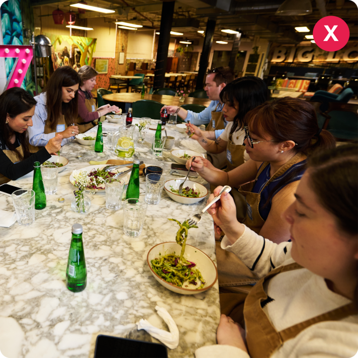 Un groupe de personnes assises autour d'une table en marbre dégustent des salades fraîches et des boissons dans un cadre intérieur animé et coloré au décor artistique.