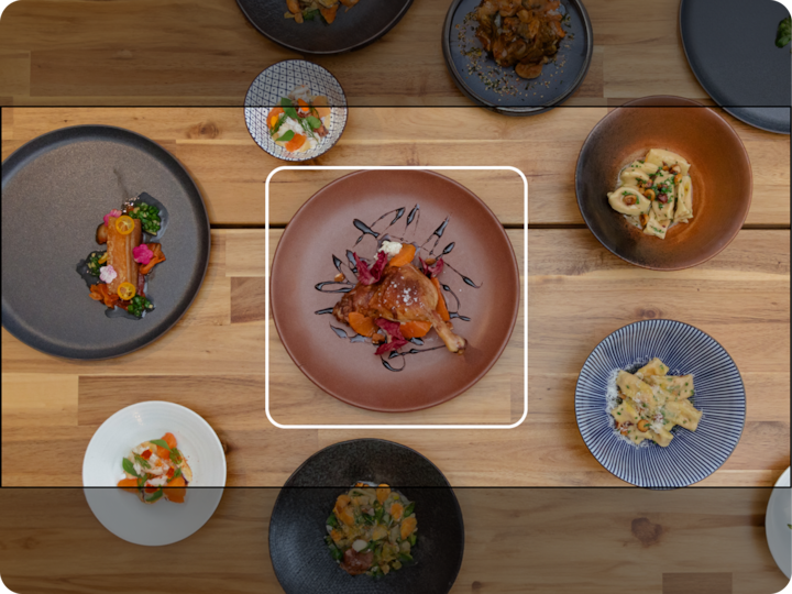 Vue plongeante sur une table en bois avec divers plats colorés, dont un plat central avec de la viande rôtie garnie de fleurs comestibles et nappée d'un glaçage balsamique.